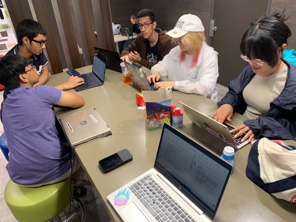 Teens gathered around a table coding on laptops at the Queens meetup